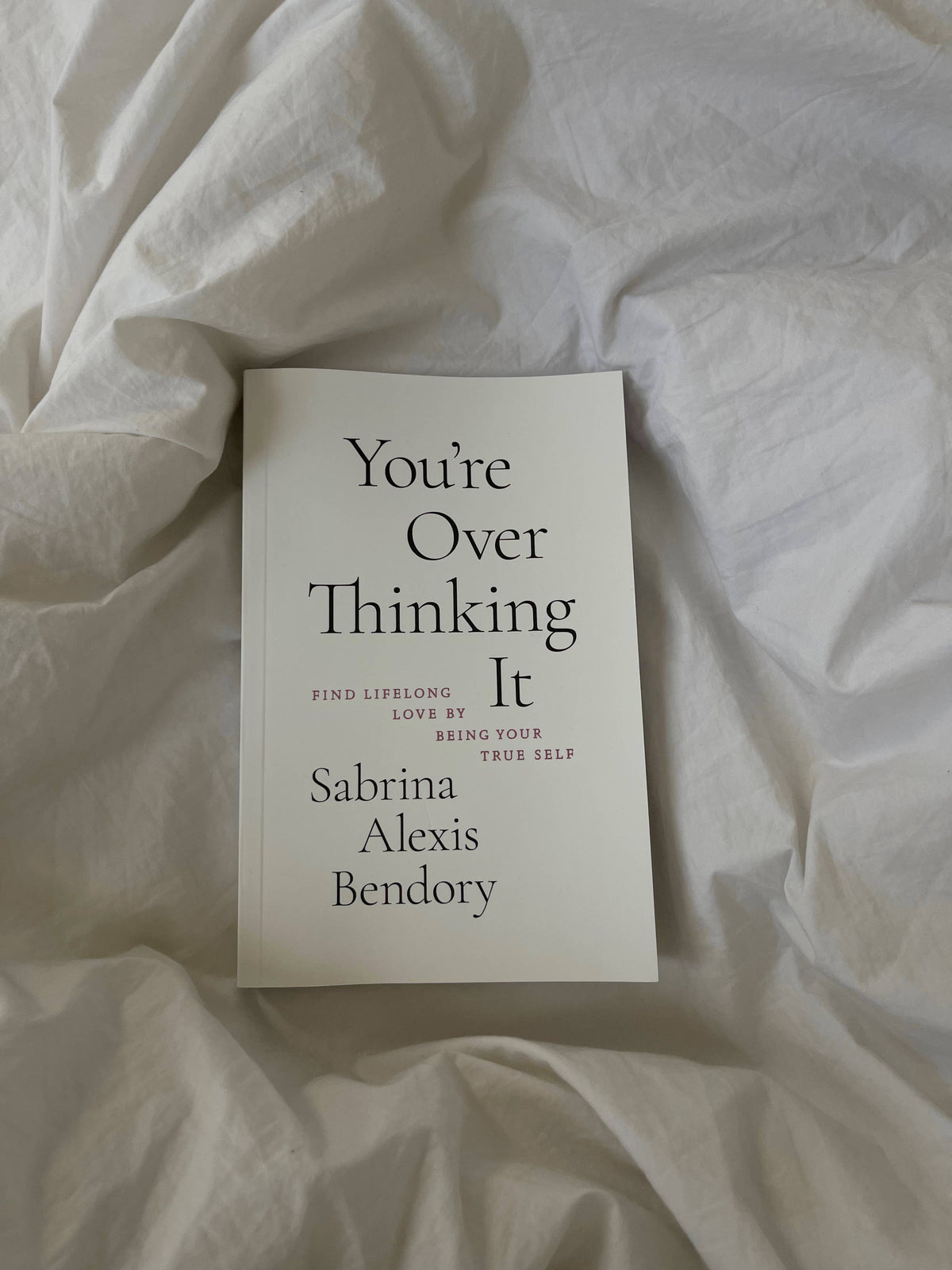 Book titled 'You're Over Thinking It' by Sabrina Alexis Bendory on a white fabric background