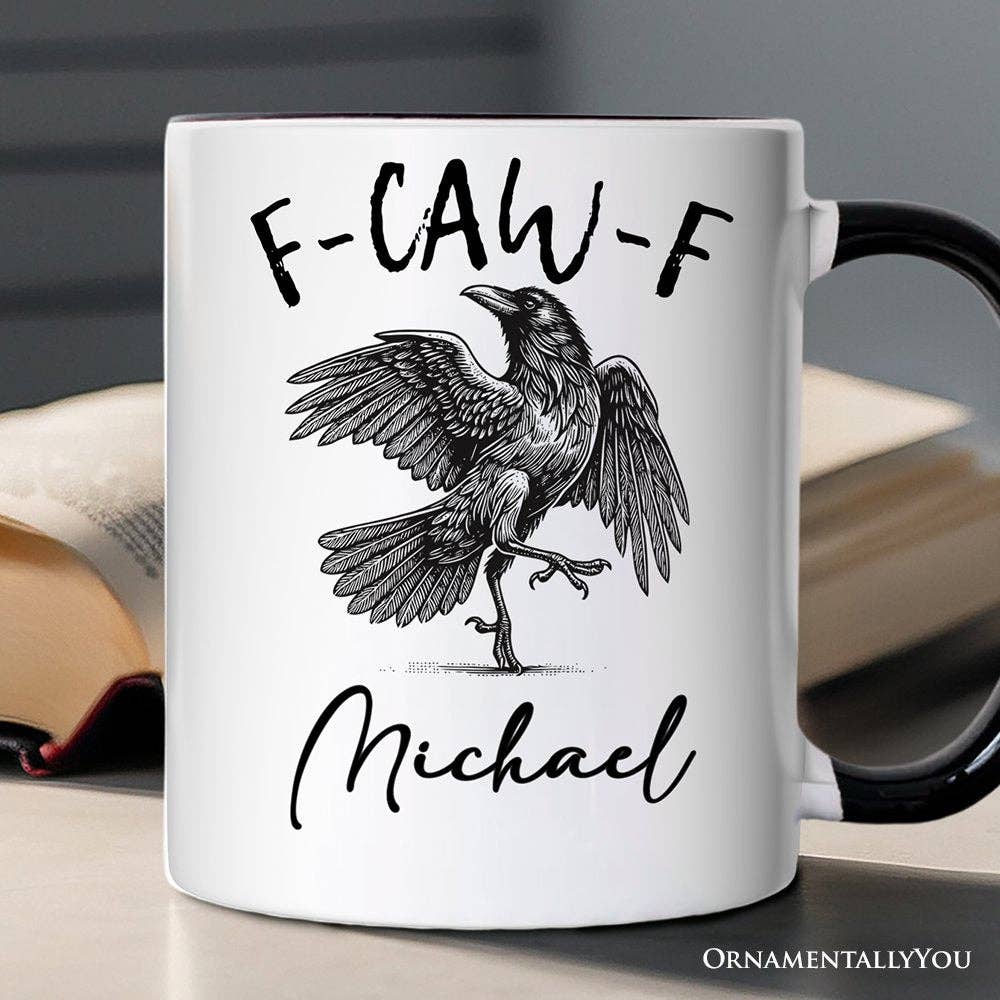 White mug with a black crow illustration and 'F-CAW-F Michael' text on a blurred background