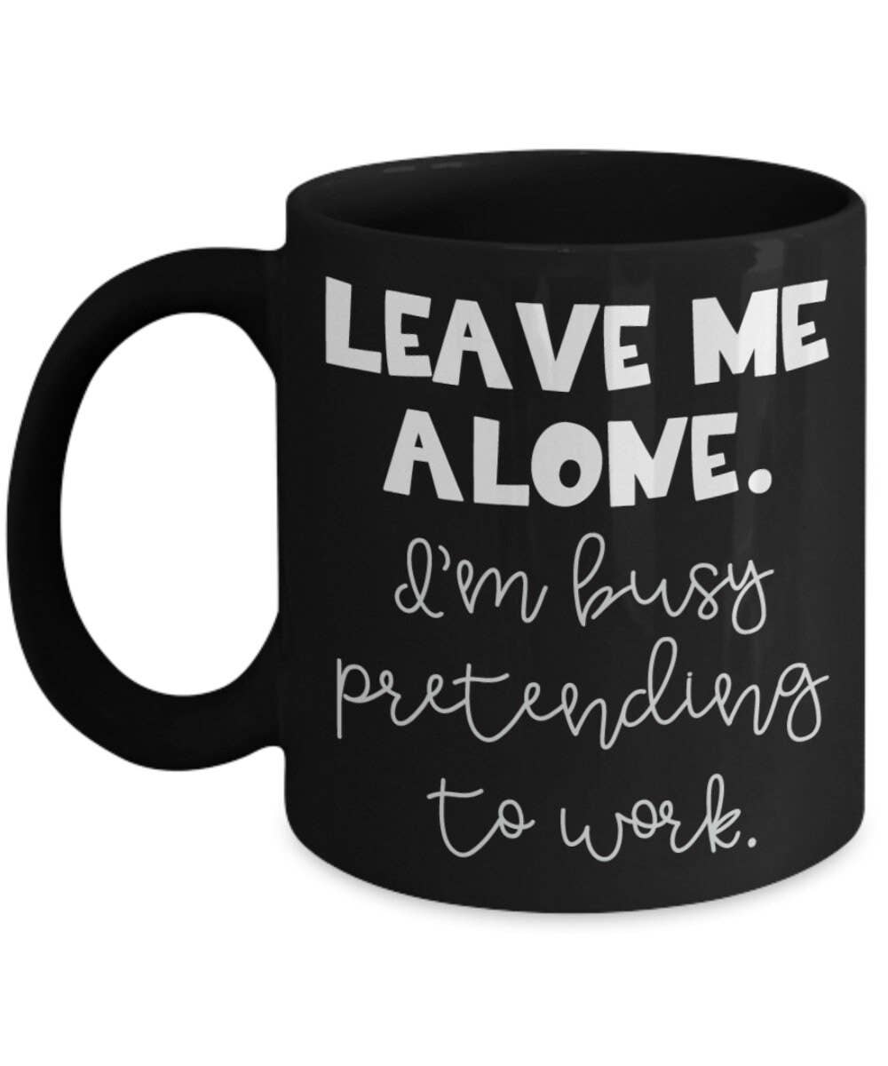 Black mug with white text 'Leave me alone. I'm busy pretending to work.' on a white background