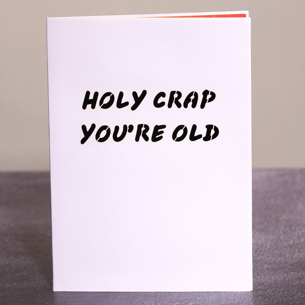 White card with black text 'HOLY CRAP YOU'RE OLD' on a gray surface.