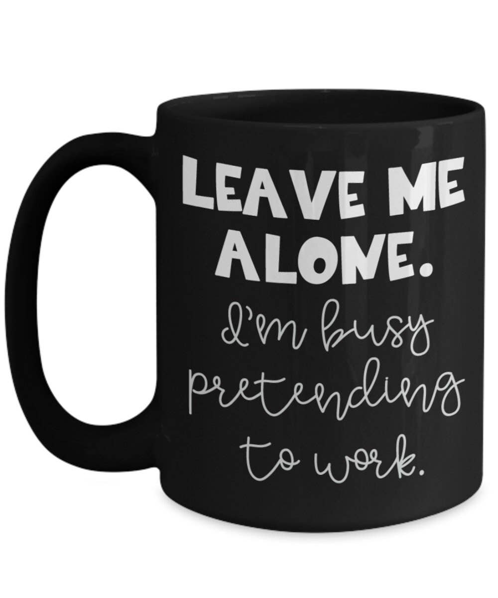 Black mug with white text 'Leave me alone. I'm busy pretending to work.' on a white background
