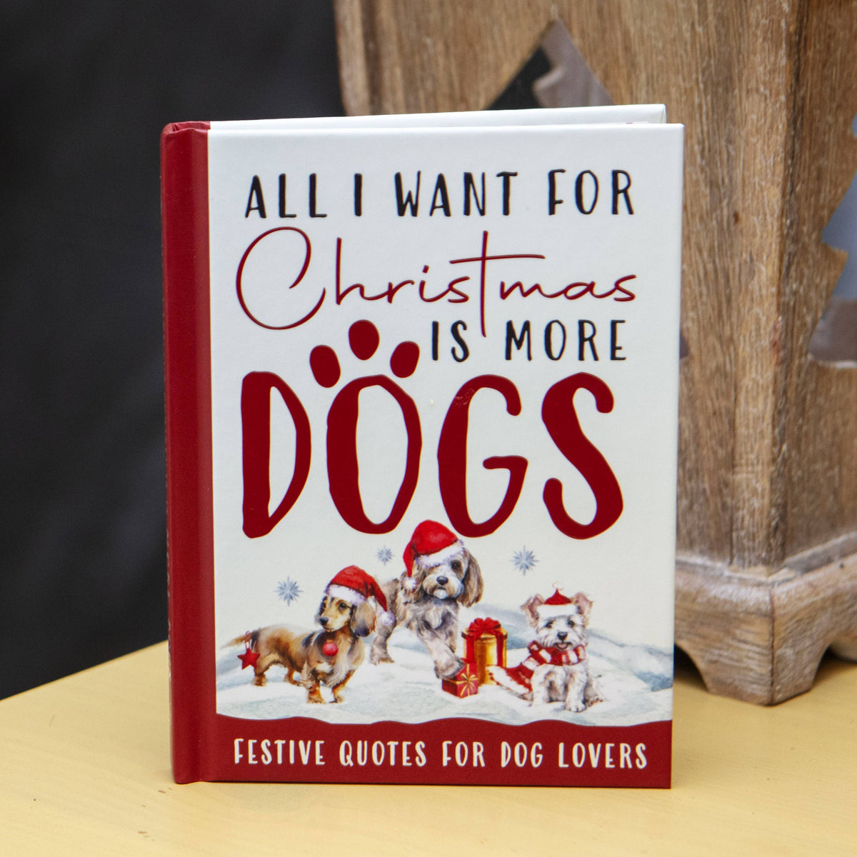 Book titled 'All I Want for Christmas is More Dogs' with festive design on a wooden surface.