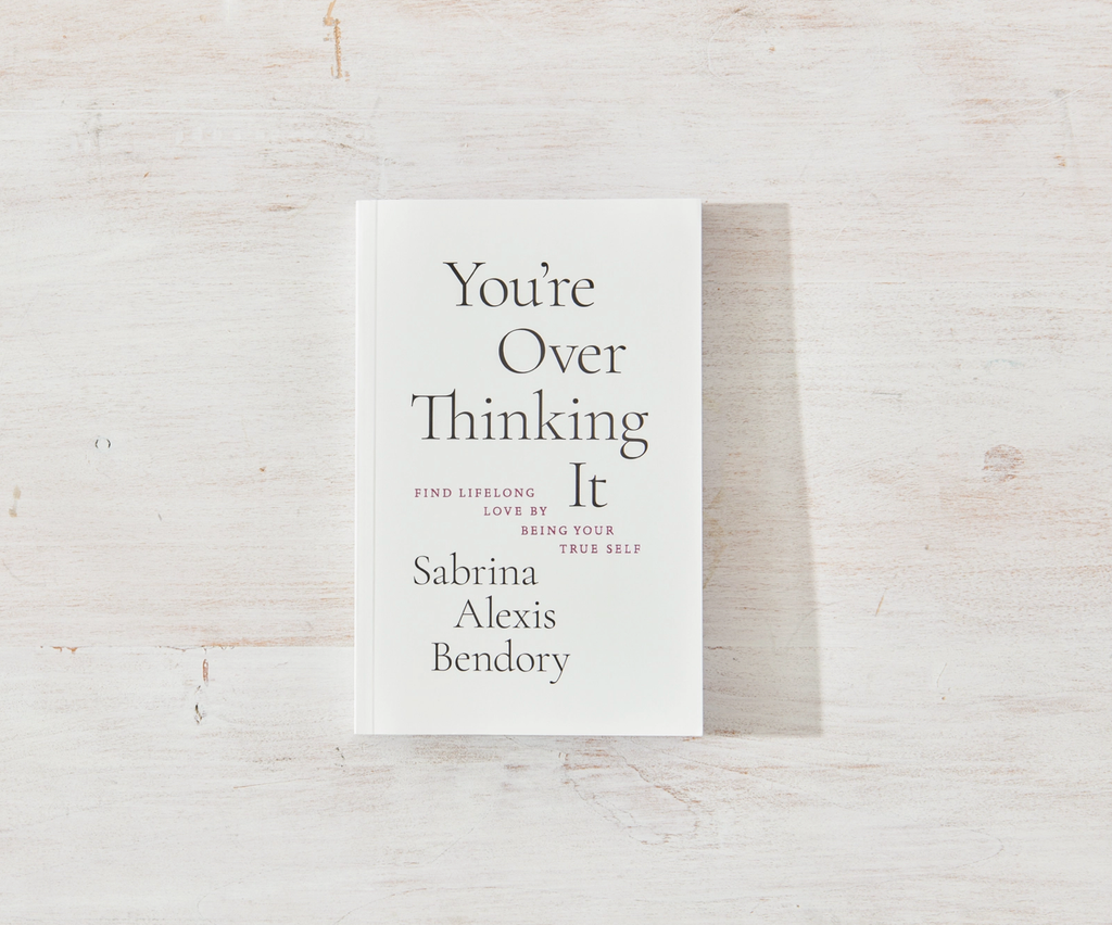 Book titled 'You're Over Thinking It' by Sabrina Alexis Bendory on a light wooden surface