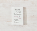 Book titled 'You're Over Thinking It' by Sabrina Alexis Bendory on a light wooden surface