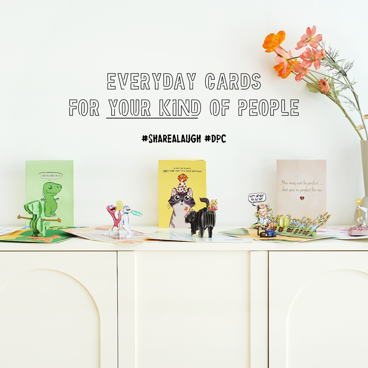 Display of greeting cards and small figurines on a white surface with text overlay.