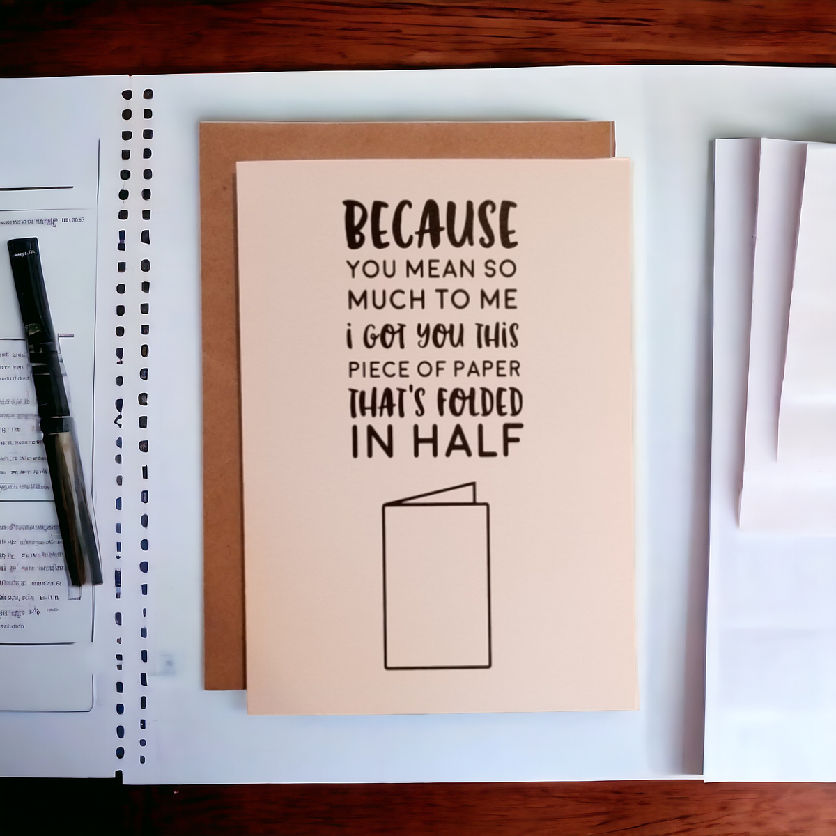 Card with humorous message on a desk with a pen and paper.