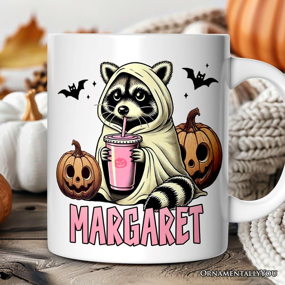 Mug with a raccoon in a costume holding a pink drink, surrounded by pumpkins and autumn decorations.