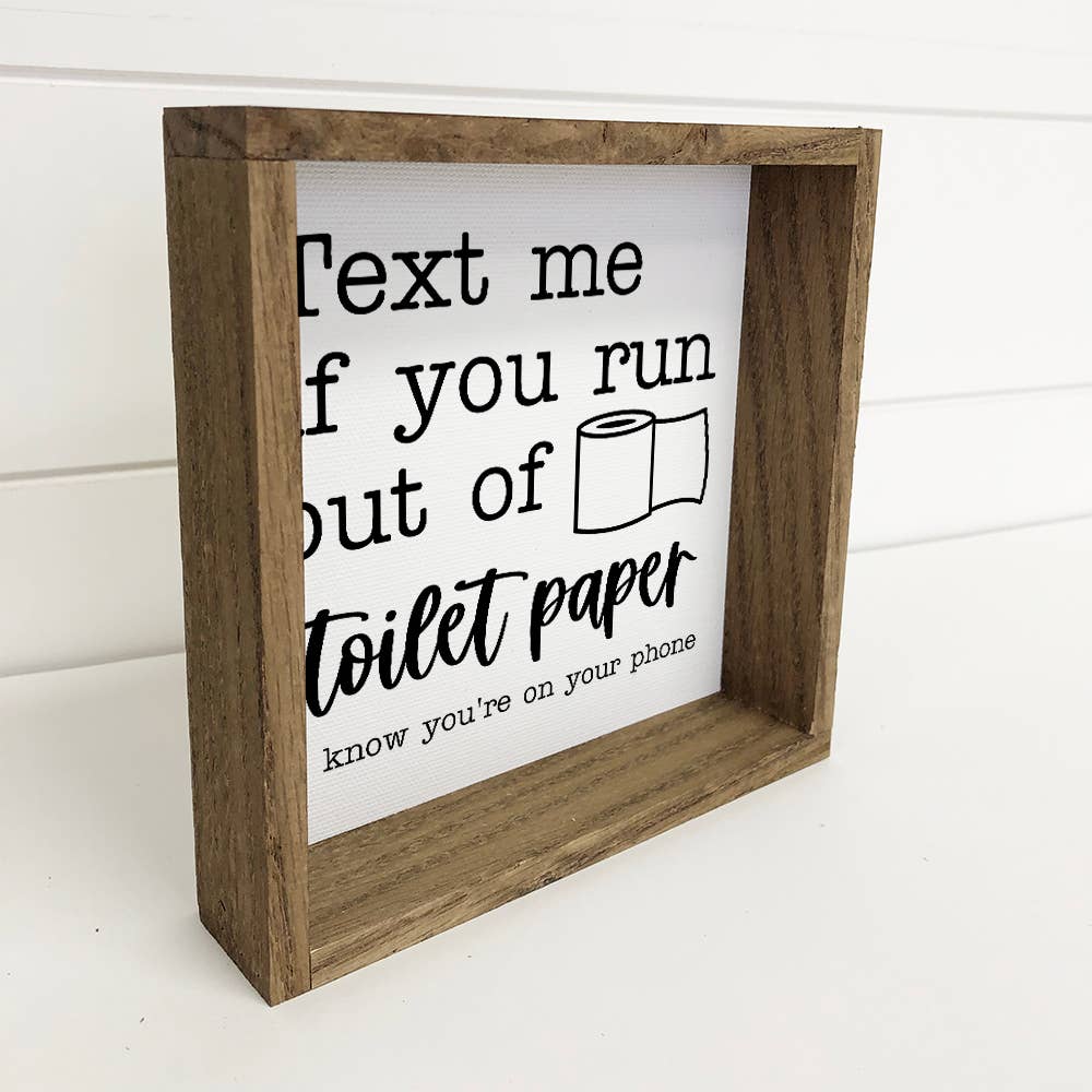 Wooden framed sign with humorous text about toilet paper and phone usage on a white background