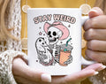 Mug with skeleton and opossum design and 'Stay Weird' text held by a person.