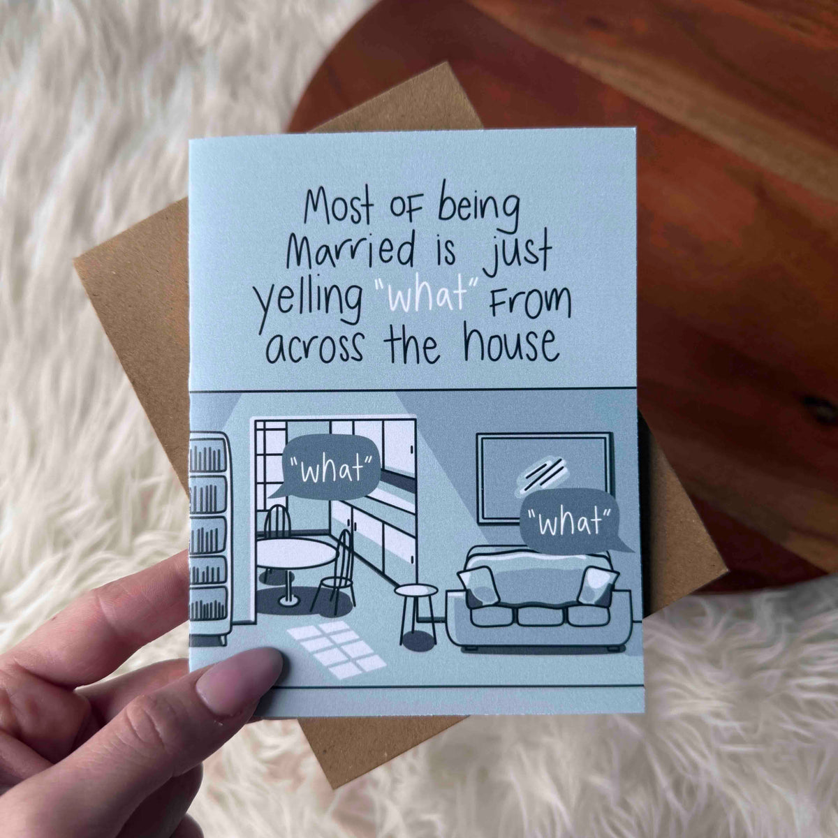 Card with humorous illustration and text about marriage, held by a hand on a soft surface.