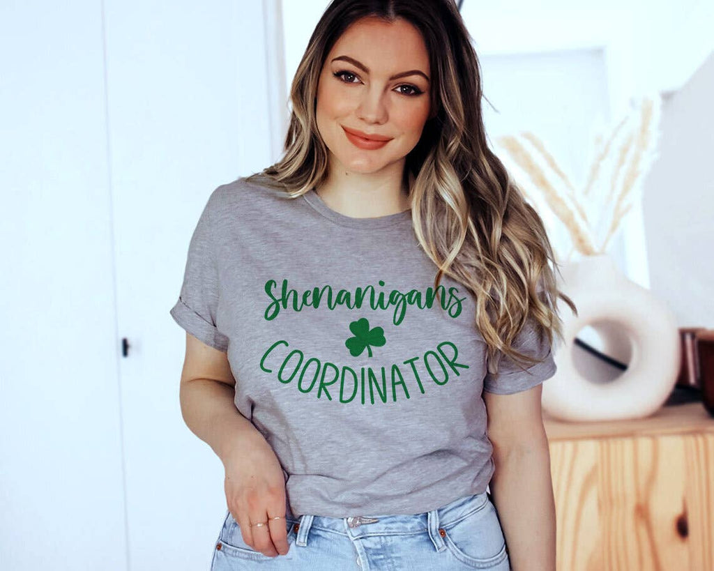 Woman wearing a gray t-shirt with 'Shenanigans Coordinator' text and shamrock graphic.