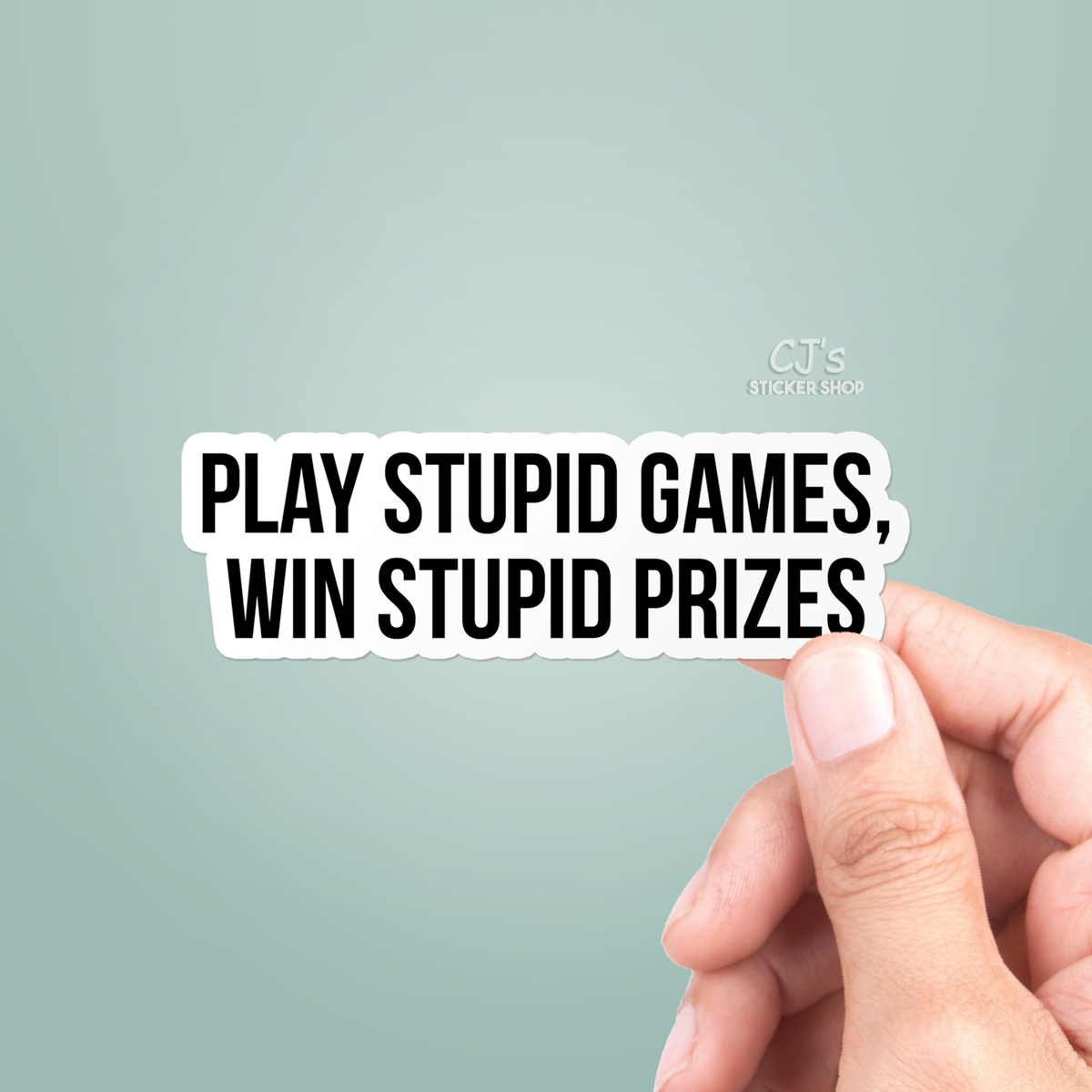 Hand holding a sticker with text 'Play Stupid Games, Win Stupid Prizes' on a light green background.