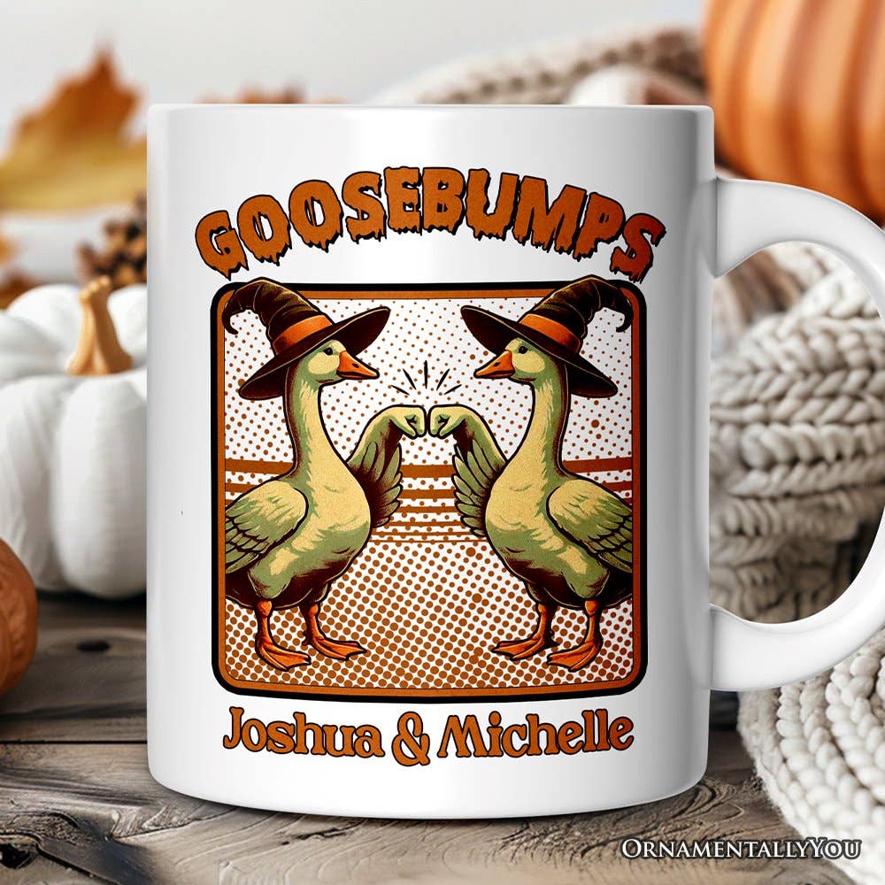 A white ceramic mug with a Halloween-themed graphic featuring two green ducks wearing orange witch hats and bumping fists under the word 'GOOSEBUMPS,' with the names 'Joshua & Michelle' printed below. The mug is styled on a rustic wooden surface with pumpkins and a knitted blanket in the background.