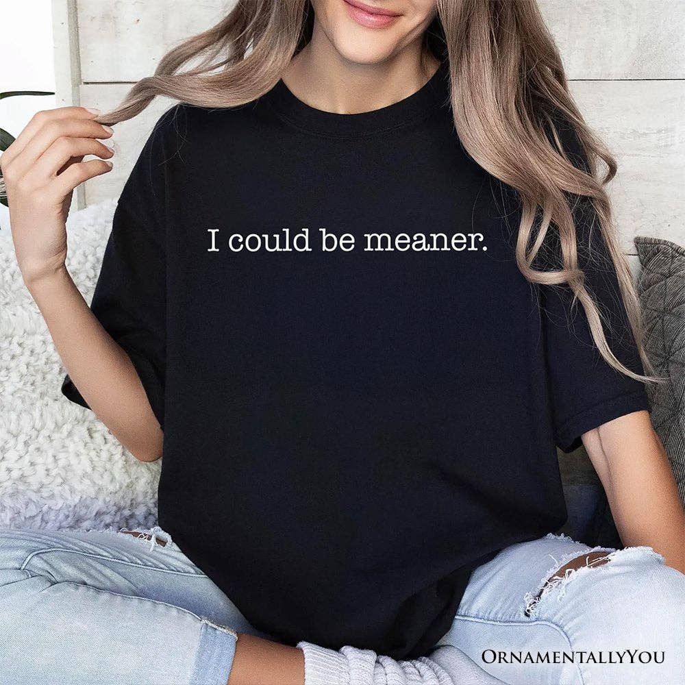Person wearing a black t-shirt with 'I could be meaner.' text, sitting on a couch.