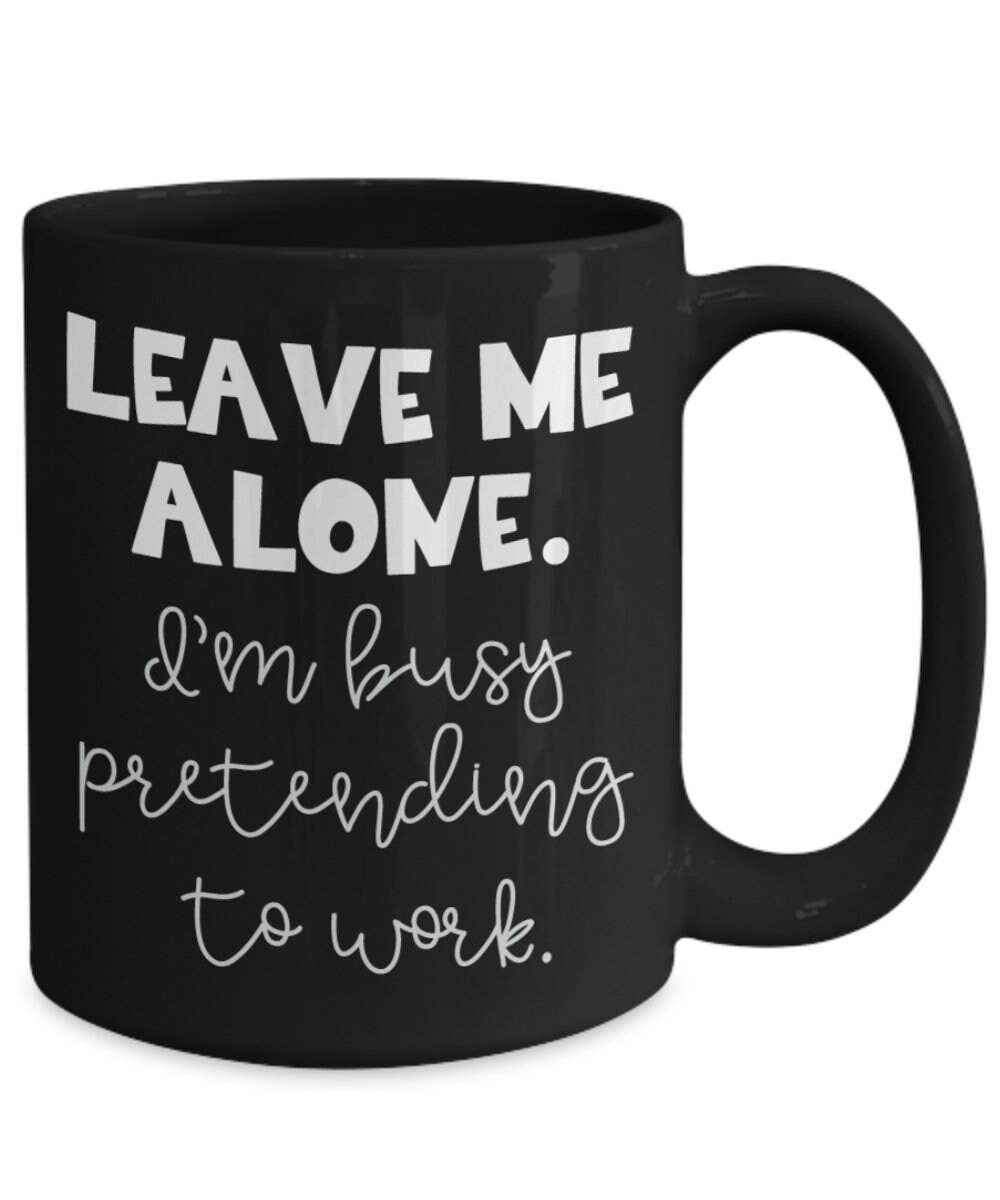 Black mug with white text 'LEAVE ME ALONE. I'm busy pretending to work.' on a white background
