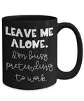 Black mug with white text 'LEAVE ME ALONE. I'm busy pretending to work.' on a white background