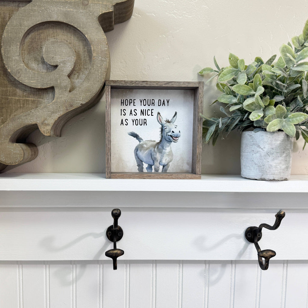 Decorative shelf with a framed picture of a donkey and text, a plant, and wall hooks.