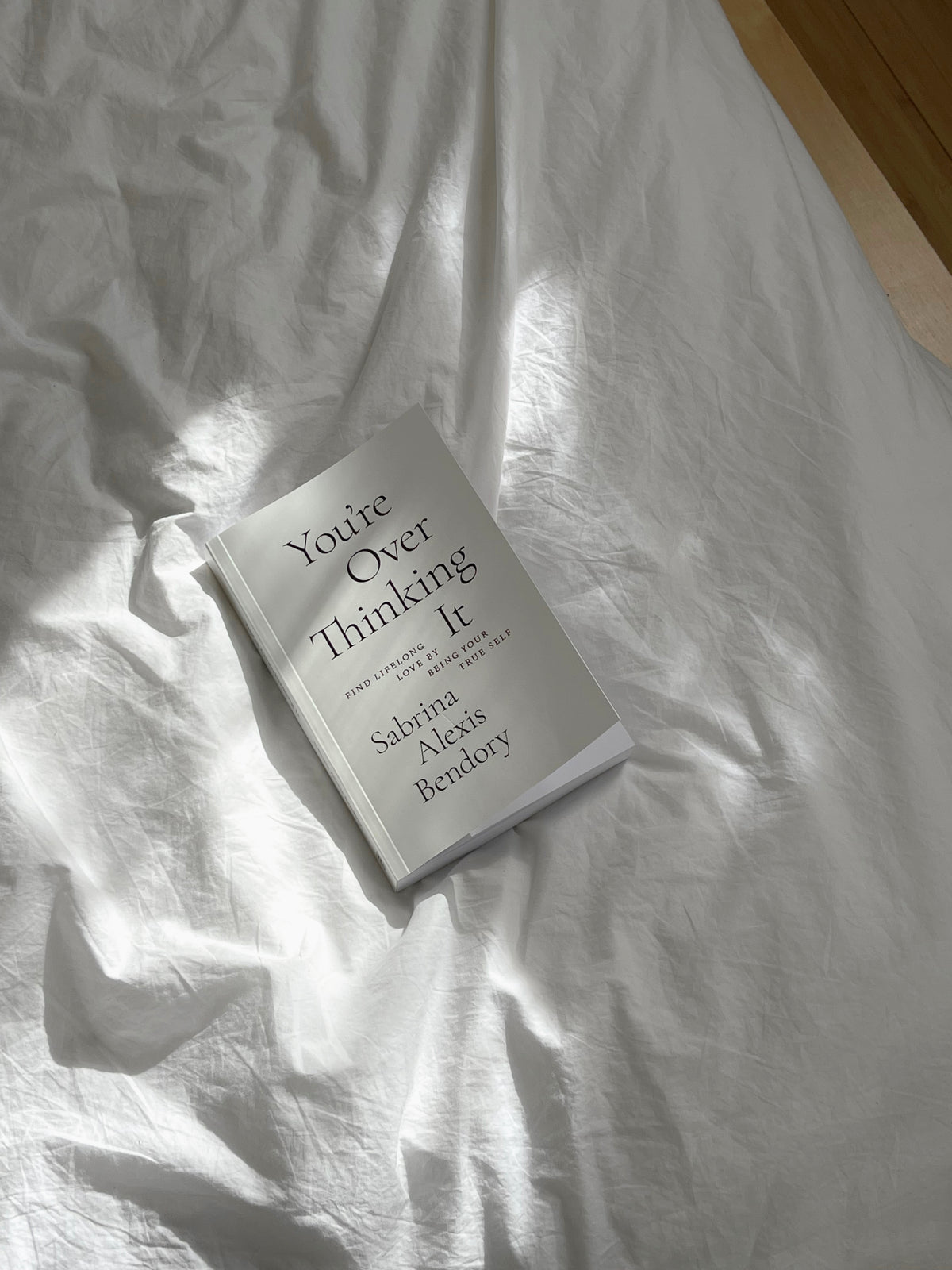 Book titled 'You're Over Thinking It' by Sabrina Alexia Bendory on a white bedspread.
