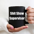 Black mug with 'Shit Show Supervisor' text held by a person against a white background