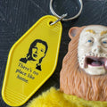 Yellow keychain with a face and text, next to a lion figurine on a dark surface