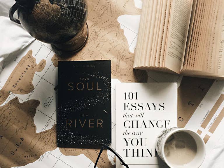 Books and a globe on a surface with a map, including 'Your Soul in a River' and '101 Essays that will Change the Way You Think'.