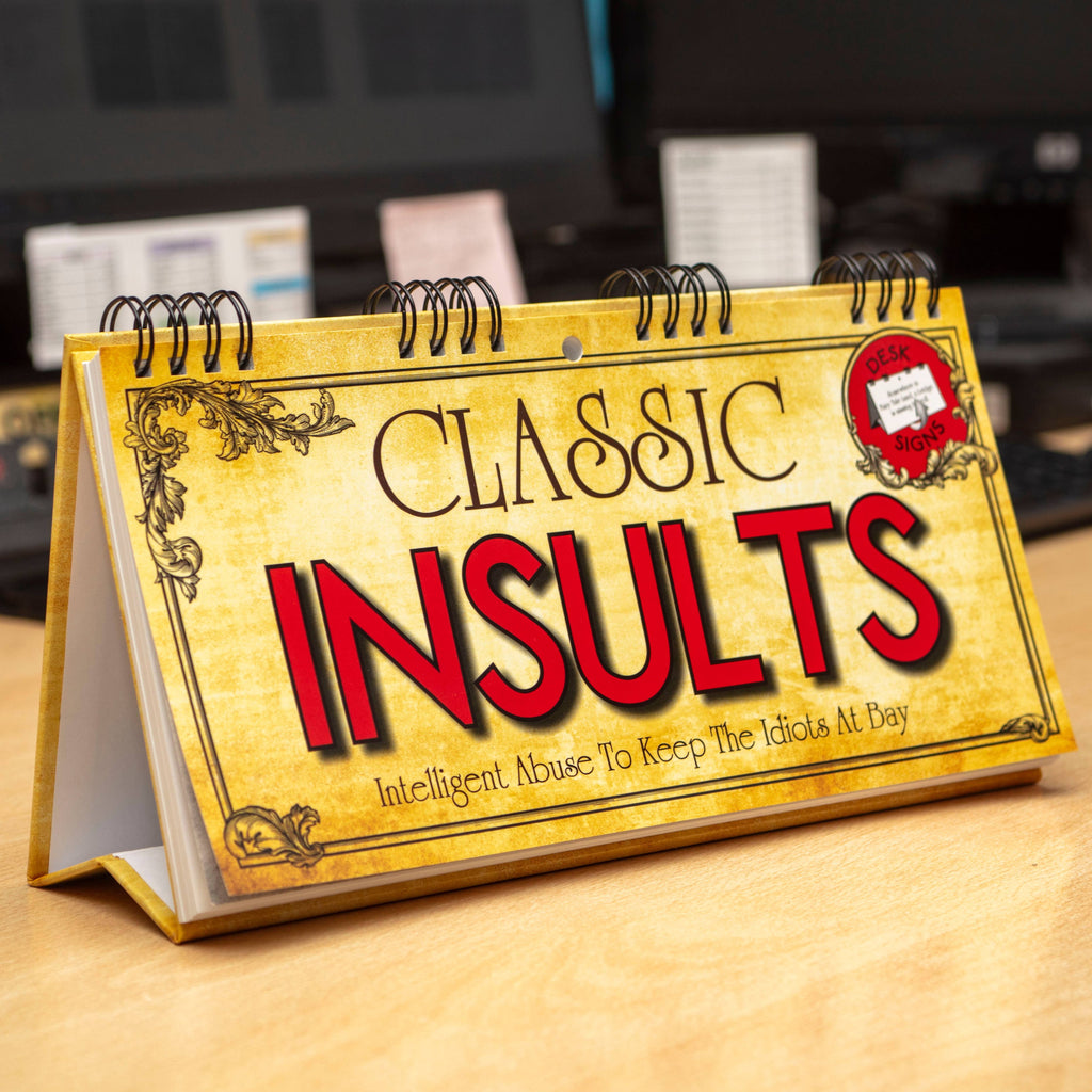 Desk calendar titled 'Classic Insults' on a wooden surface with a blurred office background.