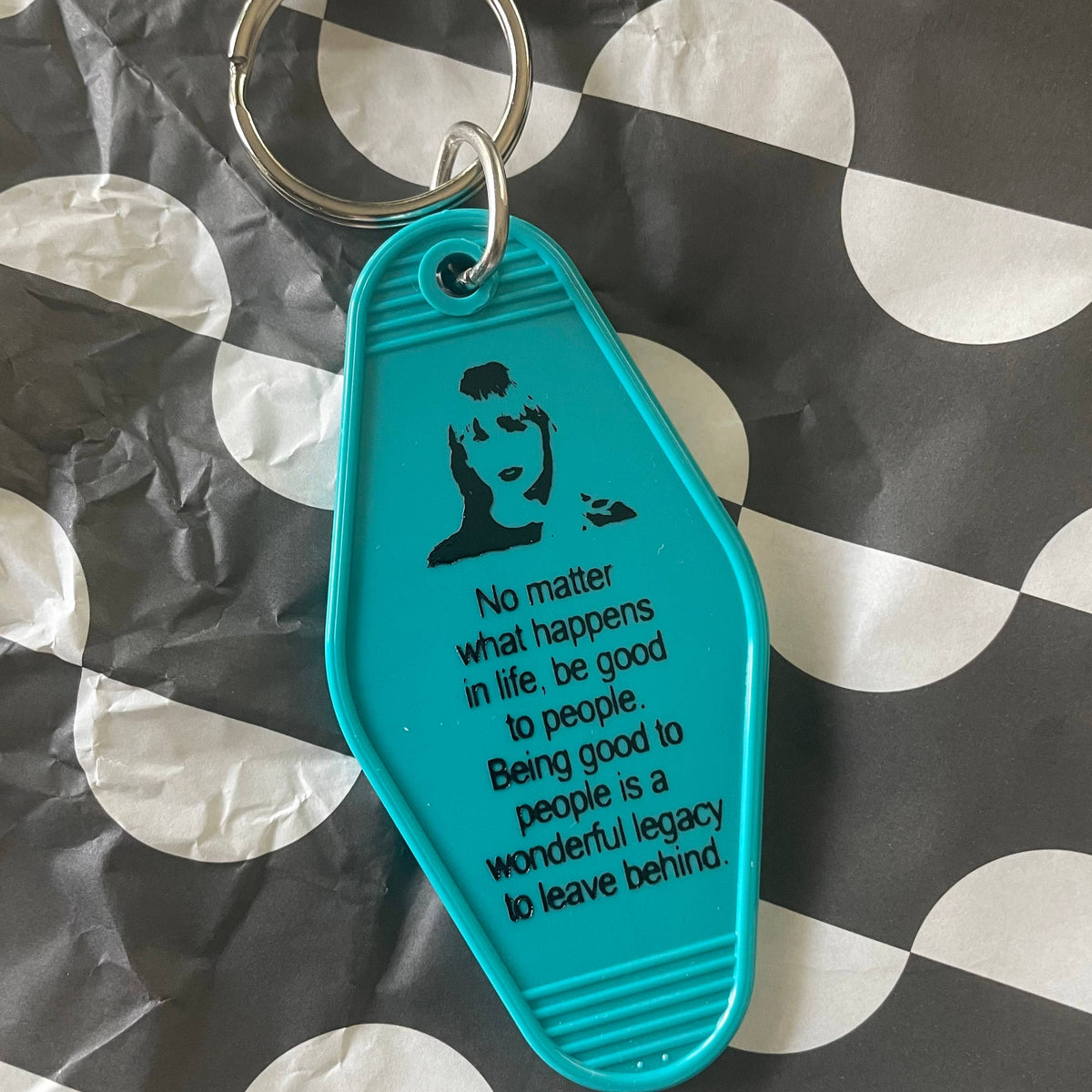 Teal keychain with motivational quote on a checkered background