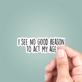 Hand holding a sticker with text 'I see no good reason to act my age' against a light blue background